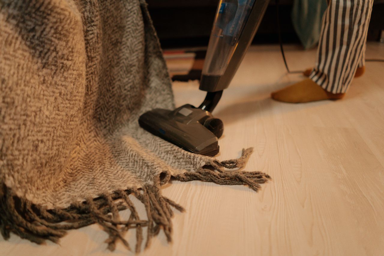 expertise-01 Close-up of vacuum cleaner cleaning a woolen blanket on the floor indoors.